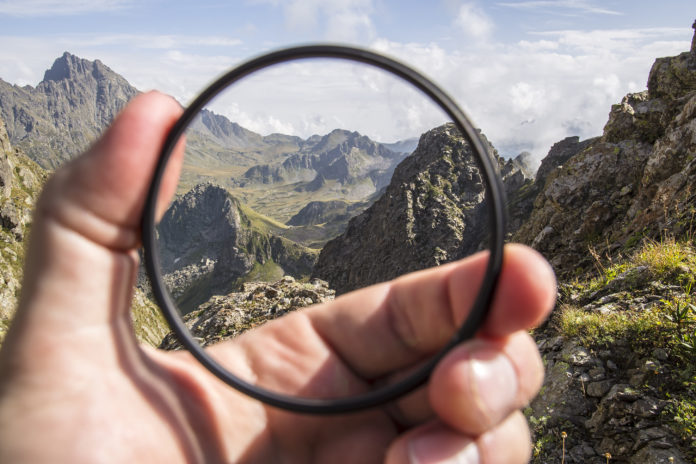 Hand puts a transparent clean protective UV filter to the camera, in the background a beautiful landscape and mountains