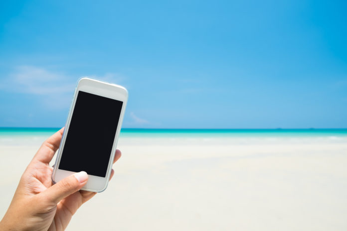 Woman hand hold white mobile phone with sea beach