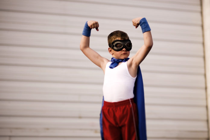 Young Boy Dressed as Supehero Flexes Biceps